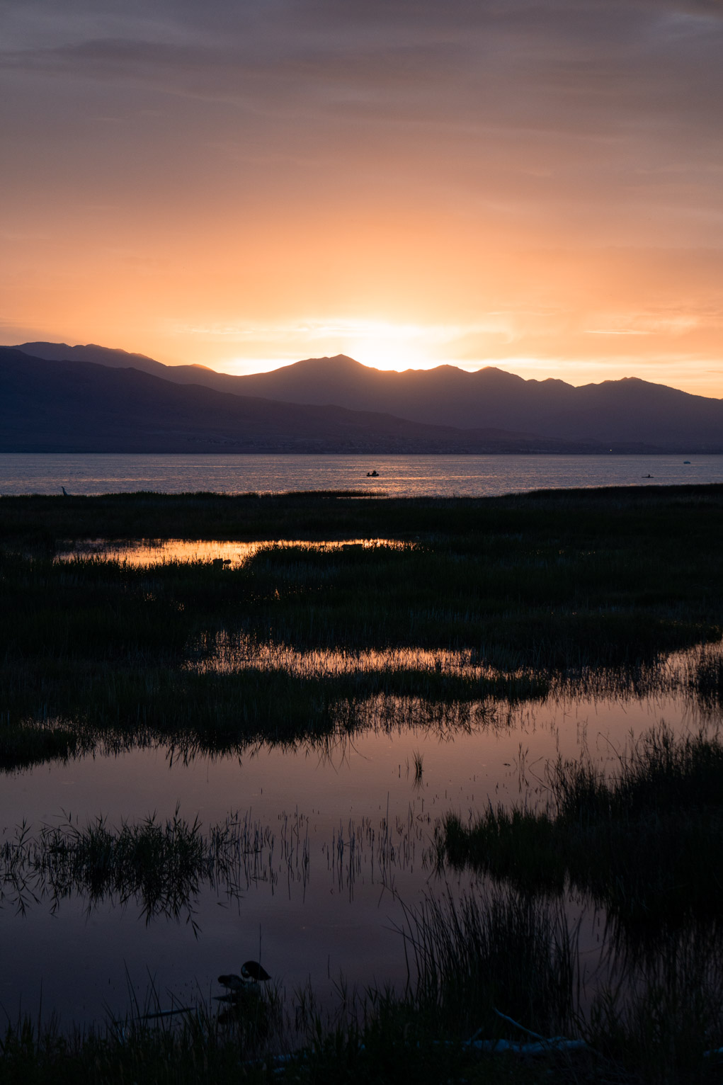 The sun sets behind blue mountains, the yellow and dusky sky is reflected in the lake